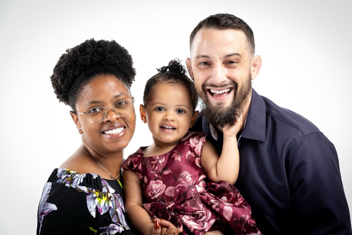 Brittani, baby Meccah, and Leo Maggio in a professional studio portrait, smiling warmly on a white background