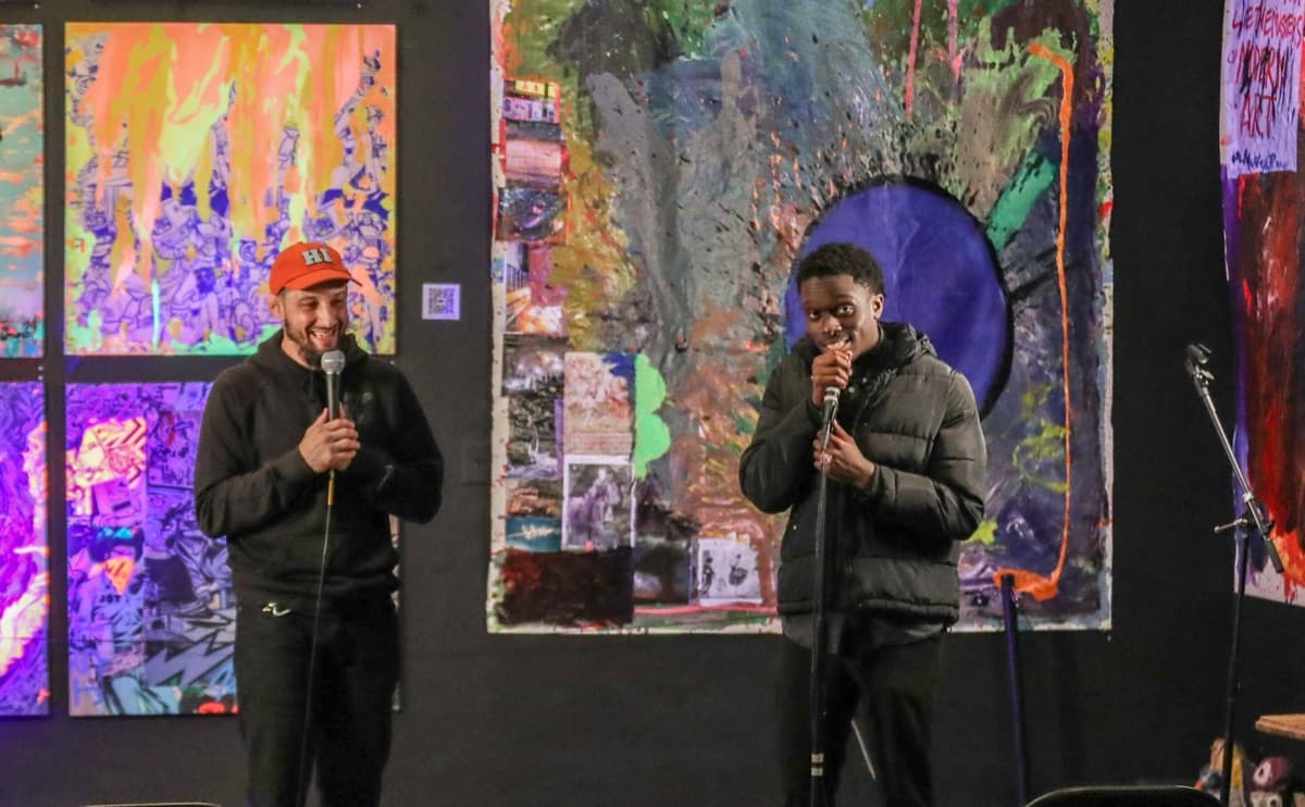 Leo hosting on stage with a microphone in front of colorful abstract art at a local community event